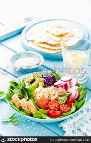 Bowl with grilled chicken meat, bulgur and fresh vegetable salad of radish, tomatoes, avocado, kale and spinach leaves. Healthy and delicious summer lunch
