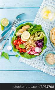 Bowl with grilled chicken meat, bulgur and fresh vegetable salad of radish, tomatoes, avocado, kale and spinach leaves. Healthy and delicious summer lunch. Top view