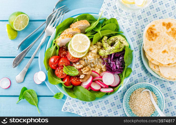 Bowl with grilled chicken meat, bulgur and fresh vegetable salad of radish, tomatoes, avocado, kale and spinach leaves. Healthy and delicious summer lunch. Top view