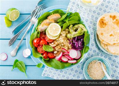 Bowl with grilled chicken meat, bulgur and fresh vegetable salad of radish, tomatoes, avocado, kale and spinach leaves. Healthy and delicious summer lunch. Top view