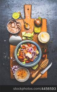 Bowl with Healthy canned Tuna fish salad ingredients : avocado, tomatoes and lime on rustic cutting board and dark background, top view