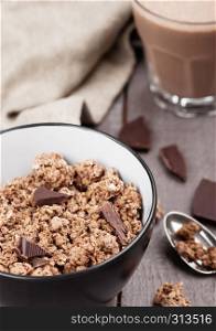 Bowl with organic chocolate granola breakfast cereal on wooden background with chocolate bar on wooden background