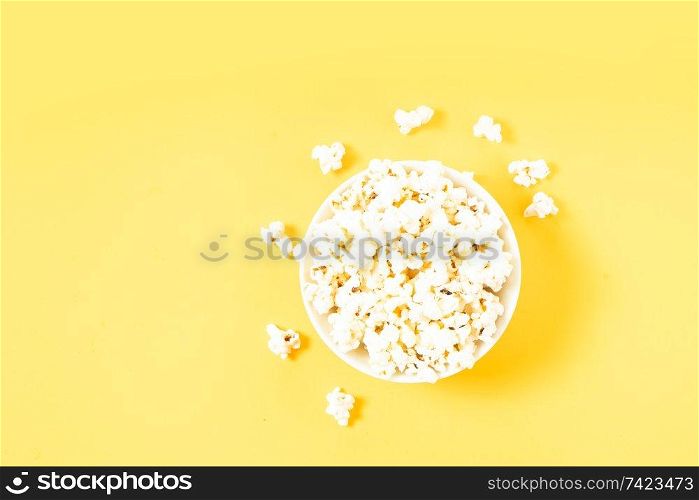 Bowl with popcorn over plain yellow background. Scattered popcorn over yellow background