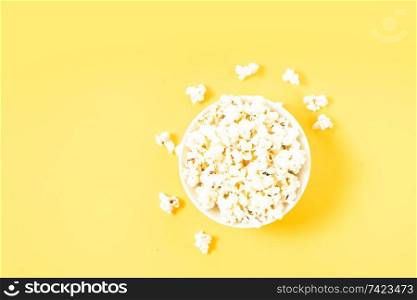 Bowl with popcorn over plain yellow background. Scattered popcorn over yellow background