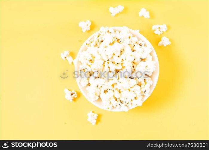 Bowl with popcorn over plain yellow desk background. Scattered popcorn over yellow background