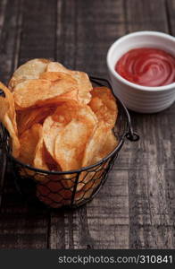 Bowl with potato crisps chips and ketchup on wooden board. Junk food
