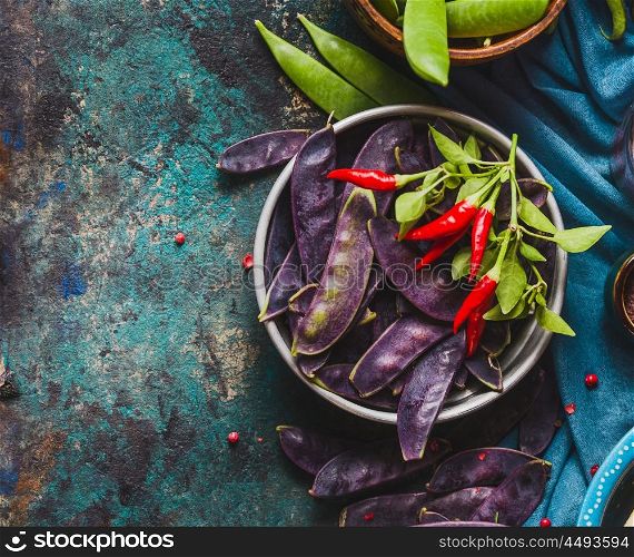 Bowl with purple pea pods and cooking ingredients on rustic background, top view