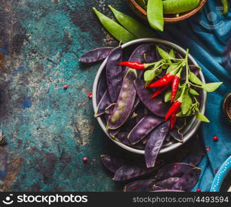 Bowl with purple pea pods and cooking ingredients on rustic background, top view