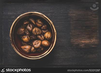 Bowl with roasted and peeled chestnuts on dark rustic background, top view, place for text