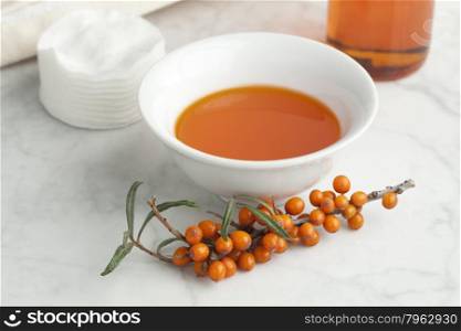 Bowl with Sea buckthorn oil with a twig of common sea-buckthorn