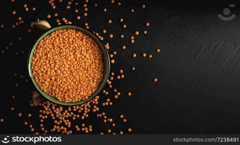 Bowl with seeds of red lentils on a black stone background. Lentil seeds and cloves of garlic are scattered next to the bowl. Flat lay. Copy space for text.