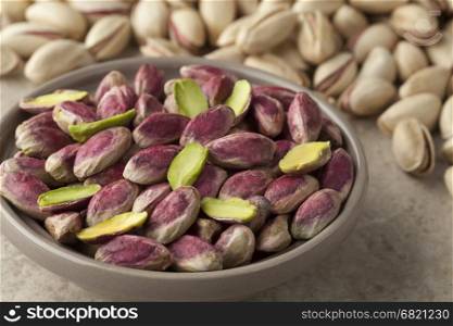 Bowl with unshelled pistachio nuts and shelled ones on the background