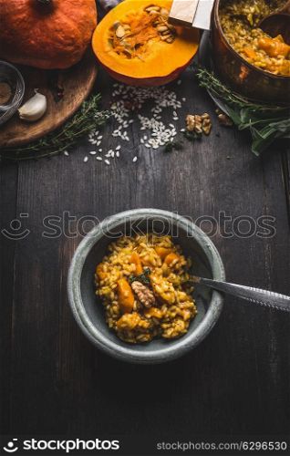 Bowl with vegetarian pumpkin risotto and spoon on dark rustic kitchen table background with cooking ingredients, top view. Healthy clean seasonal food and eating concept