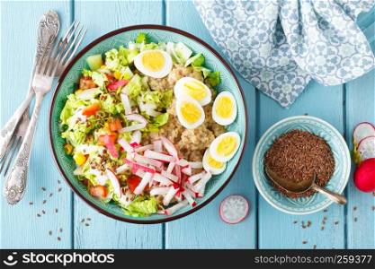 Bowl with wheat porridge, boiled quail eggs and fresh vegetable salad of radish, corn, sweet pepper and chinese cabbage. Healthy and delicious dietary lunch. Vegetarian, vegan food. Top view. Flat lay