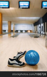 Bowling ball and house shoes on wooden floor in club, pins on background, nobody. Bowl game concept, tenpin. Bowling ball and house shoes on wooden floor