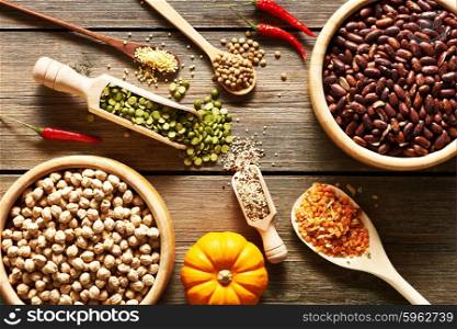 Bowls and spoons of various legumes on wooden background