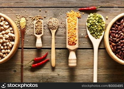 Bowls and spoons of various legumes on wooden background