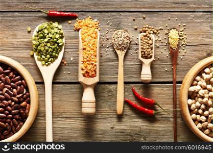 Bowls and spoons of various legumes on wooden background