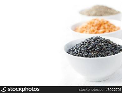 Bowls of assorted dried lentils with red lentils, black beluga lentils and mountain lentils over white
