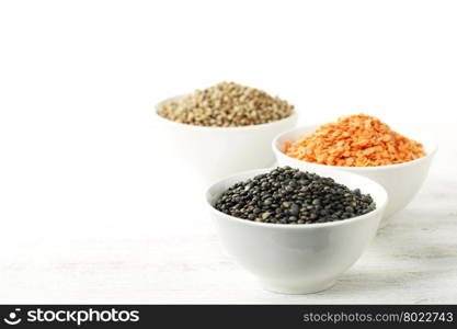Bowls of assorted dried lentils with red lentils, black beluga lentils and mountain lentils over white