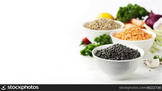 Bowls of assorted dried lentils with vegetables over white