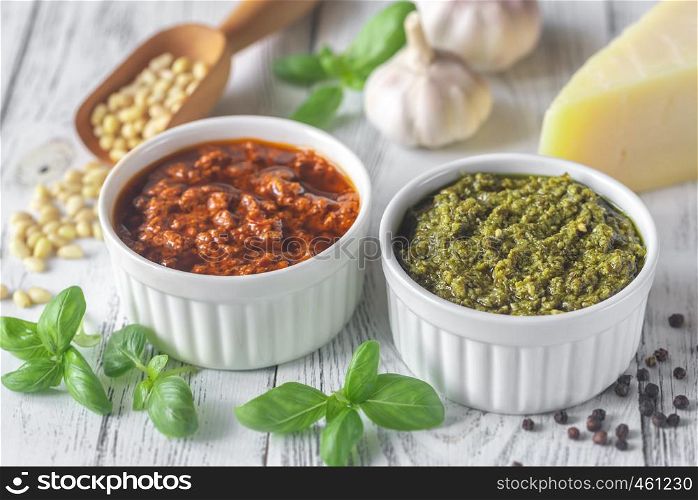Bowls of classic and sun-dried tomato pesto with ingredients on the white wooden background