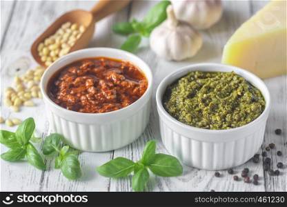 Bowls of classic and sun-dried tomato pesto with ingredients on the white wooden background