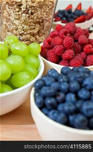 Bowls of healthy breakfast blueberries, raspberries, grapes, strawberries and granola or muesli, the focus is on the raspberries.