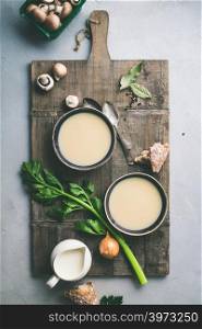 Bowls of homemade mushroom soup and ingredients on grey concrete background, top view