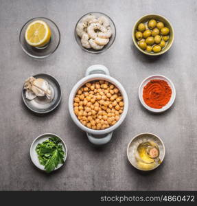 Bowls with Chickpeas salad ingredients: cooked Chickpeas, olives, shrimps, lemon, Paprika powder, herbs,olives oil on gray concrete background, top view, flat lay
