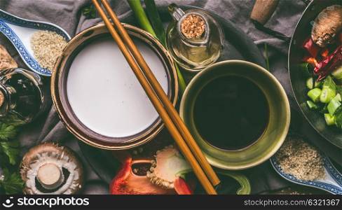Bowls with coconut milk, soy sauce, sesame oil, chopsticks and vegetables on kitchen table background, top view. Asian food cooking ingredients, Chinese or Thai cuisine concept