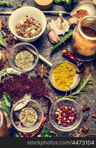 Bowls with colorful dried ground spices on old aged scored wooden background in a country kitchen, top view