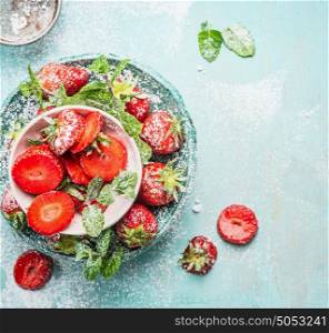 Bowls with sliced Strawberries with powdered sugar and mint leaves on light blue rustic background, top view