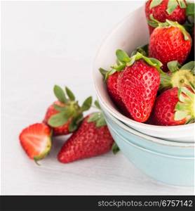 Bowls with strawberries on white table background.