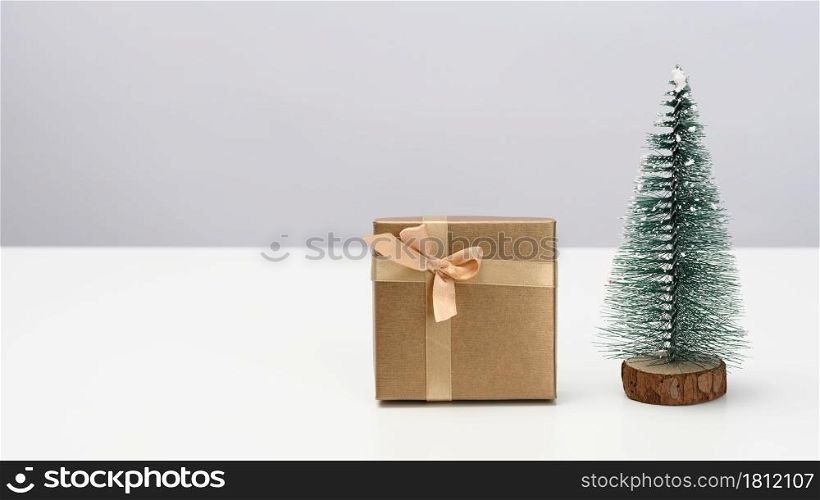 box is wrapped in brown paper and a decorative Christmas tree on a white table. Festive background, copy space