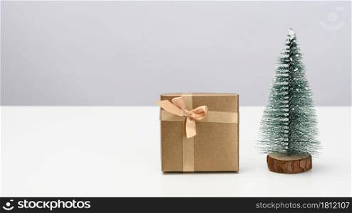 box is wrapped in brown paper and a decorative Christmas tree on a white table. Festive background, copy space