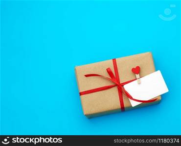 box is wrapped in brown paper and tied with a red thin silk ribbon on a blue background, copy space, holiday is Valentine&rsquo;s Day