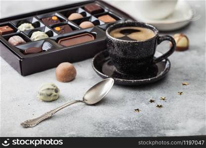 Box of Luxury Chocolate candies selection with cup of black coffee and silver spoon on light background.