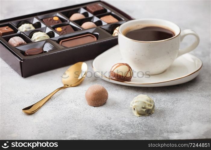 Box of Luxury Chocolate candies selection with cup of black coffee and golden spoon on light background.