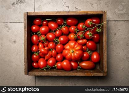 Box of mix red tomatoes in summer day. Composition of variety fresh tomatoes. Gray tile background. Top view.. Mix red tomatoes