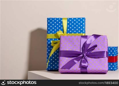 box packed in festive purple paper and tied with silk ribbon on a beige background, birthday gift, surprise
