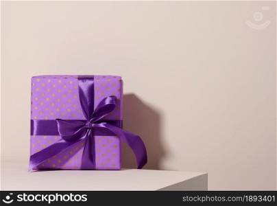 box packed in festive purple paper and tied with silk ribbon on a beige background, birthday gift, surprise