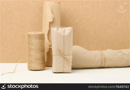 box, roll of brown kraft paper and reel with brown rope on white table, packing material, zero waste