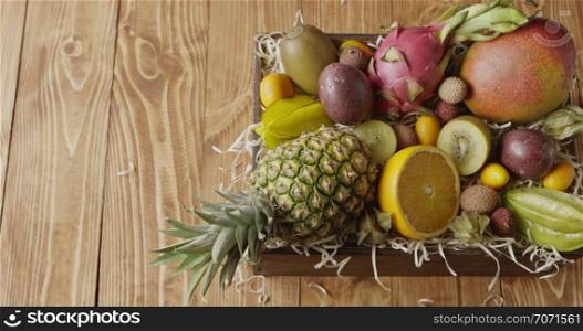Box with assortment of freshly picked natural exotic fruits -ananas, passion fruit, mango on a wood shaving on a wooden background. Panoramic slow motion, 4K UHD video, 3840, 2160p. Top view.. Panoramic video top view on a box with variety fresh natural organic exotic fruits on a wooden background. Slow motion, 4K UHD video, 3840, 2160p.