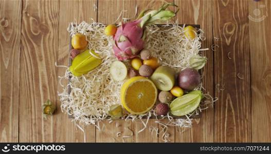Box with assortment of freshly picked natural exotic fruits on a wooden background. Girl&rsquo;s hand puts ananas, passion fruit, mango on a wood shaving. Motion, 4K UHD video, 3840, 2160p.. Top view woman&rsquo;s hand puts natural organic mango, pineapple, kiwi in a the box with variety exotic tropic fruis on a wooden table. Motion, 4K UHD video, 3840, 2160p.