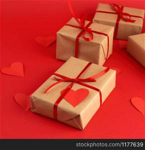 box wrapped in brown kraft paper and tied with a red thin silk ribbon, cut out of paper hearts, red background, gift for Valentine&rsquo;s Day, birthday, flat lay