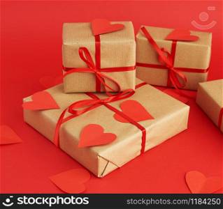 box wrapped in brown kraft paper and tied with a red thin silk ribbon, cut out of paper hearts, red background, gift for Valentine&rsquo;s Day, birthday