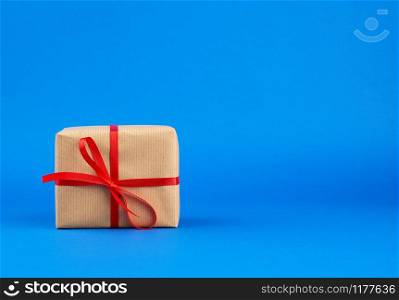 box wrapped in brown paper and tied with a red bow, gift on a blue background. Great design for any purposes. Holiday background. Valentine gift.