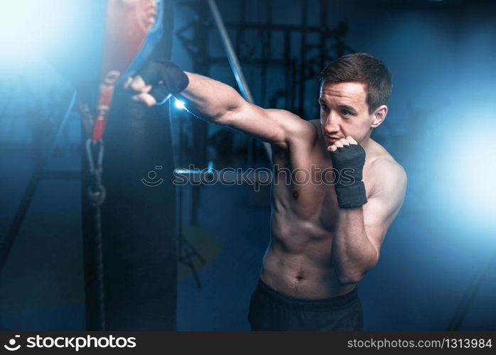 Boxer in bandages training with bag in gym. Boxing workout, mens sport