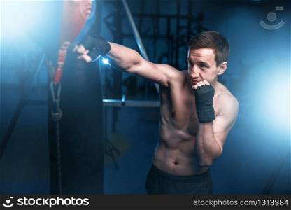 Boxer in bandages training with bag in gym. Boxing workout, mens sport